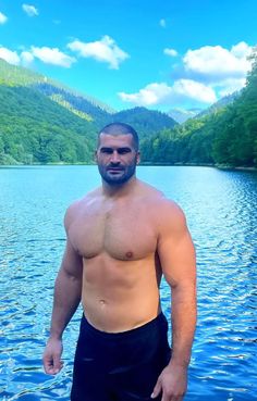 a shirtless man standing in front of a body of water with mountains in the background