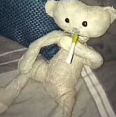 a white teddy bear sitting on top of a bed holding a toothbrush in it's mouth