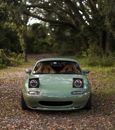 a green sports car is parked in the woods