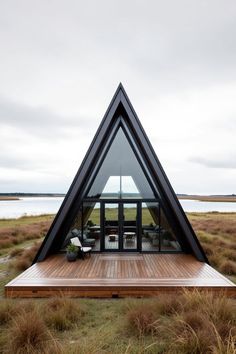 a triangular shaped house sits in the middle of a field with grass and water around it