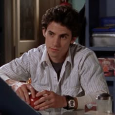 a young man sitting at a table with an apple in his hand and looking away from the camera