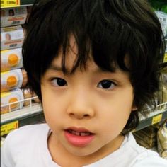 a young child with fake eyelashes on her head in a grocery store aisle looking at the camera