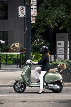 a woman riding on the back of a green scooter down a city street