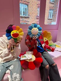 two people sitting on a bench with stuffed animals in front of them and one person holding a cell phone