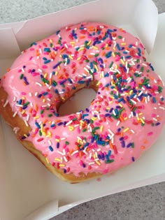 a pink frosted donut with sprinkles in a box