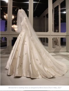 a wedding dress on display in front of large windows