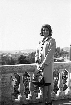 a woman standing on top of a balcony next to a railing holding a handbag
