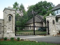 an iron gate in front of a brick house with a driveway and trees behind it