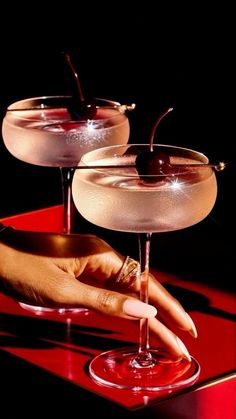 two martinis sitting on top of a red table with one being filled with liquid