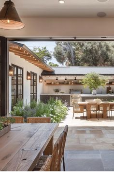 Bright, airy outdoor dining area with a wooden table, surrounded by lush greenery and a modern open kitchen, creating a welcoming space for entertaining.