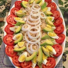 a platter filled with sliced tomatoes, avocado and onion on top of a checkered table cloth