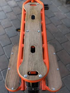 an orange and black bike handlebars with wood on the front end, sitting on a brick sidewalk