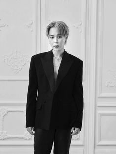 a woman standing in front of a white wall wearing a black jacket and pants with her hands in her pockets