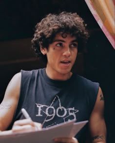 a young man with curly hair is holding a clipboard