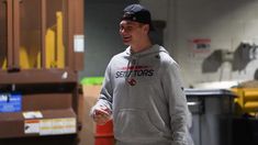 a man in a gray hoodie is holding a red frisbee and smiling