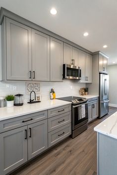 a kitchen with gray cabinets and white counter tops, stainless steel appliances and an island