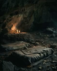 there are two candles that are lit in the dark cave with rocks and leaves on the ground