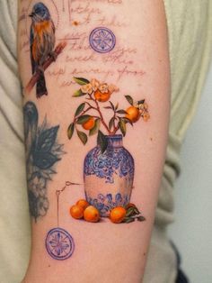 a tattoo with oranges and flowers in a vase on someone's left arm
