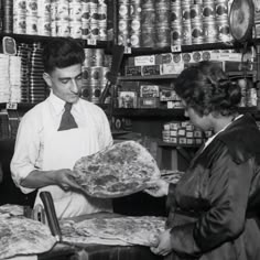 an old black and white photo of two people in a store holding up some pizza