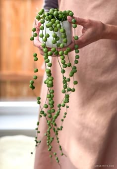 a woman holding a white vase filled with green beads and greenery hanging from it's side