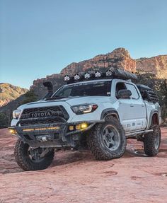 a white toyota truck parked on top of a rocky hill with mountains in the background