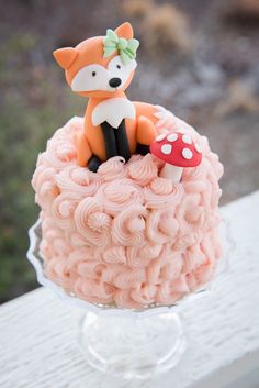 a small cake with pink frosting and a fox figurine sitting on top
