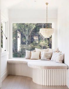 a large window seat with pillows on it in front of a white wall and wooden floor