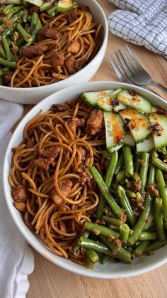 two white bowls filled with noodles and veggies next to each other on top of a wooden table
