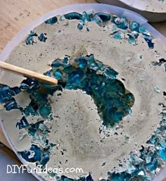 a blue and white cake sitting on top of a pan covered in frosting next to a wooden spatula