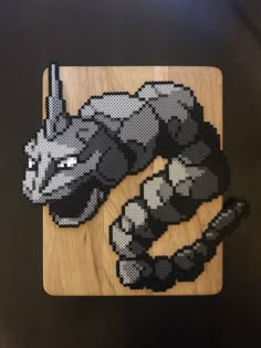 an animal made out of perler beads on a wooden cutting board with the image of a cat laying down