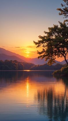 the sun is setting over a lake with trees in front of it and mountains in the distance