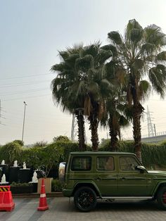 a green jeep is parked in front of some palm trees and orange cones on the sidewalk