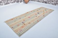 a rug on the floor in front of a brick wall with a vase next to it