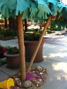 a palm tree made out of paper sitting on the ground next to a potted plant