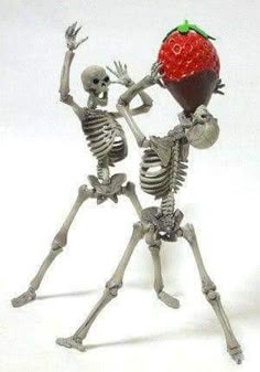 two skeleton figurines holding up a strawberry