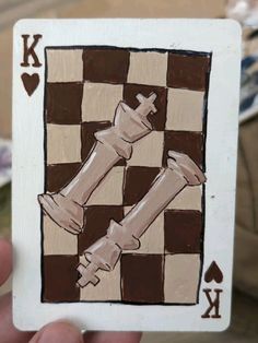 a hand holding up a playing card with chess pieces painted on the front and sides