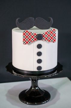 a white cake with a red bow tie and mustaches on top is sitting on a black stand