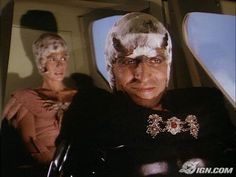 two people sitting in the back of an airplane, one wearing a headdress