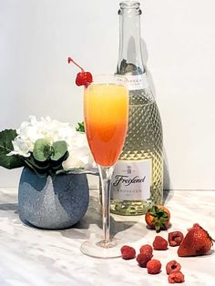 a bottle of champagne next to a glass with strawberries and flowers in front of it
