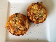 two muffins sitting on top of a white plate covered in cheese and sauce