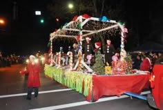 a parade float with christmas decorations on it and people standing around in the street at night