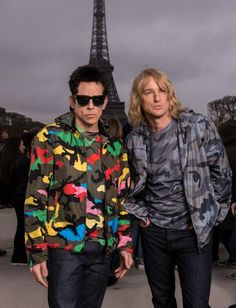 two young men standing next to each other in front of the eiffel tower
