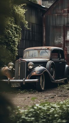an old car is parked in front of a rusty building with trees and bushes around it