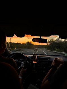 two people driving down the road at sunset with their cell phones in their hand and one person on the steering wheel