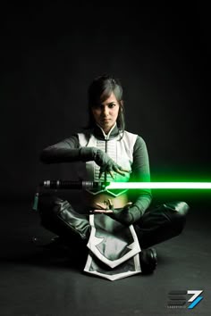 a woman sitting on the ground holding a green light saber