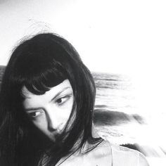 a woman with long hair standing in front of the ocean