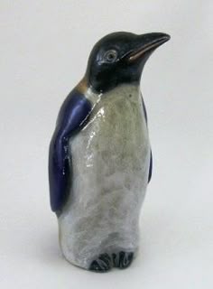 a ceramic penguin figurine sitting on a white surface with its head turned to the side