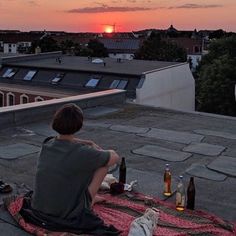 a man sitting on top of a roof next to bottles of beer