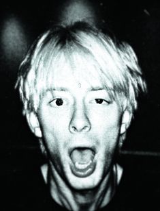 a black and white photo of a young man with his mouth open in front of the camera