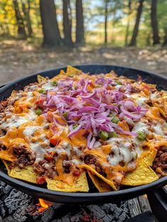 nachos with meat, cheese and onions on an outdoor fire pit in the woods
